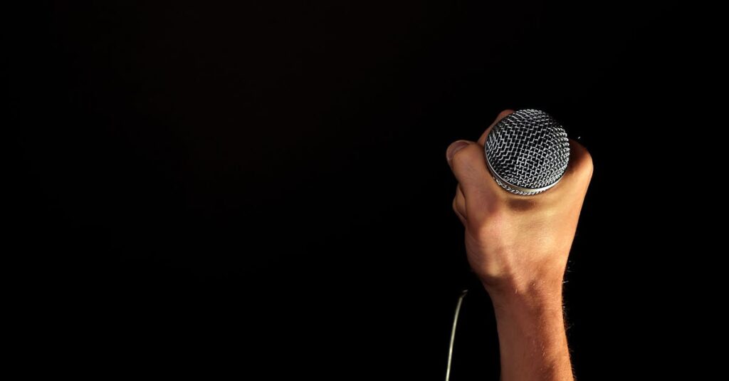 Close-up of a hand firmly gripping a microphone against a dark backdrop.